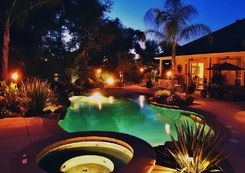 A pool with lights and plants around it